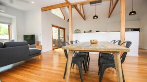 Un vaste espace de vie comprenant une table à manger en bois, des chaises noires, un canapé gris et un téléviseur en arrière-plan.