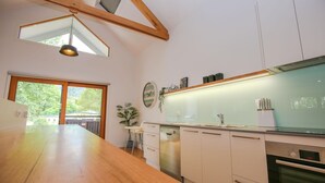 Une cuisine moderne dotée d’un plan de travail en bois, de meubles blancs, d’un four encastré et d’une grande fenêtre donnant sur un paysage verdoyant.