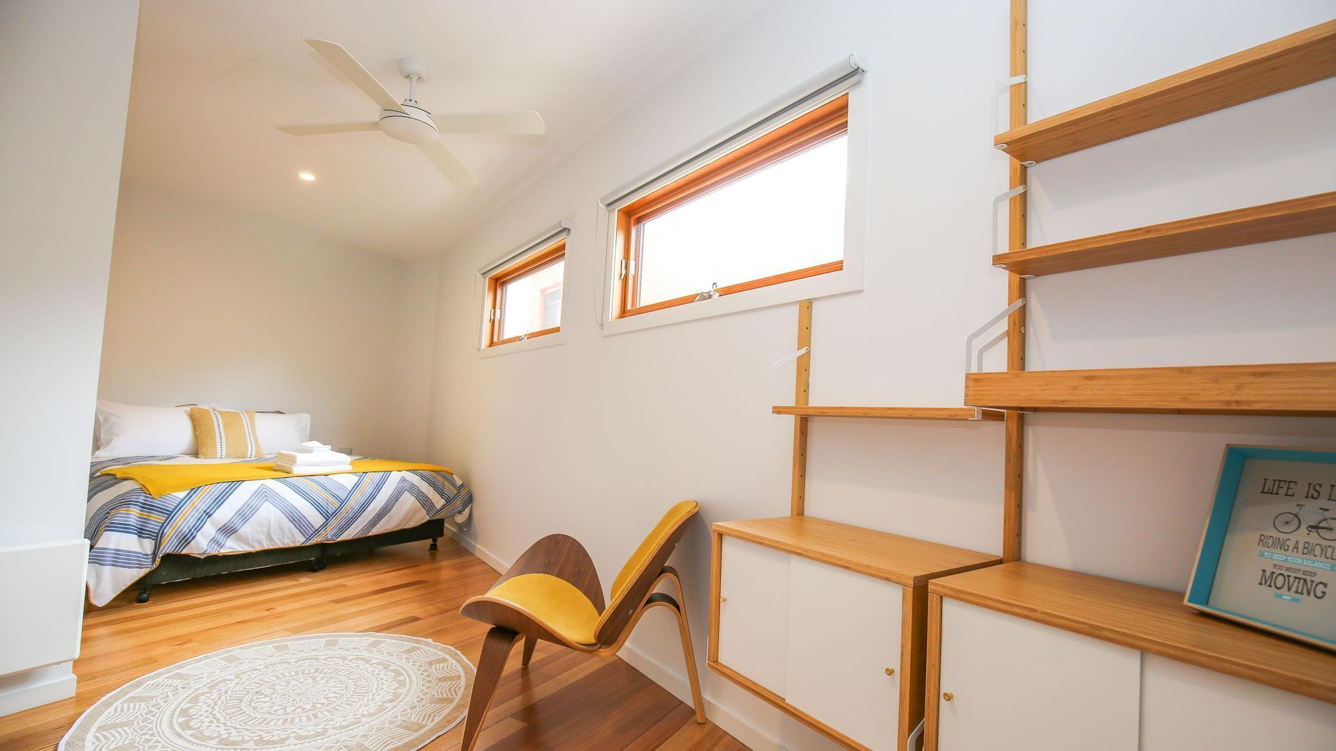 A bedroom with a bed, a chair, a desk, and built-in shelving.