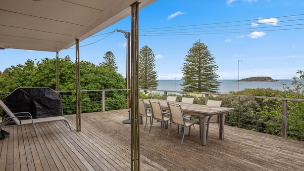 A wooden deck with a table and chairs, overlooking a body of water and a distant island.