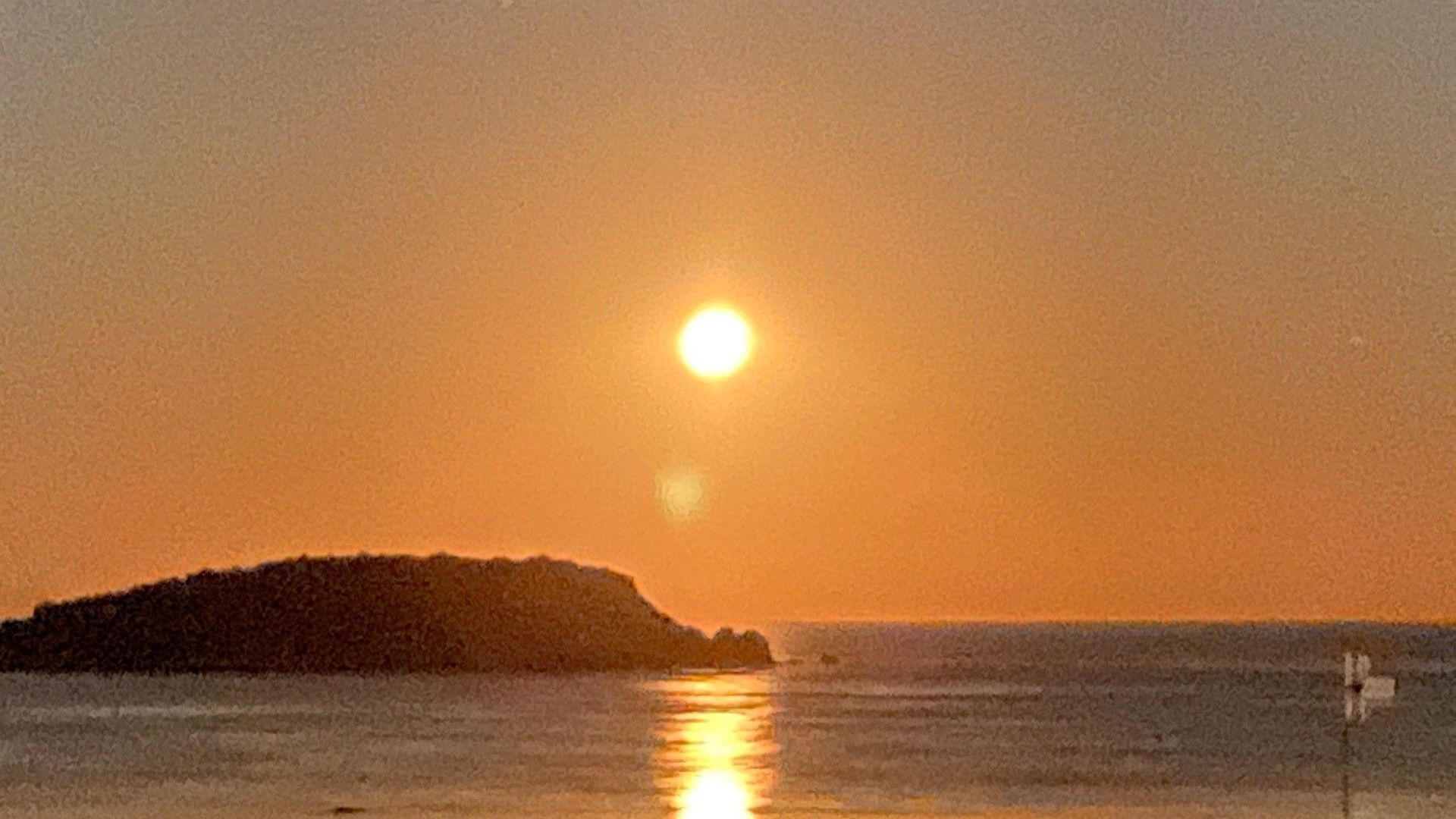 Un coucher de soleil sur une étendue d’eau, avec une petite portion de terre au premier plan.