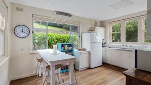 A kitchen with a dining area, a clock, and a view of greenery.