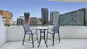 A balcony with two chairs and a table, overlooking a cityscape with modern buildings. - North Sydney - BS901 Berry Street - Modern 1BR with Balcony in the Heart of North Sydney CBD (North Sydney)