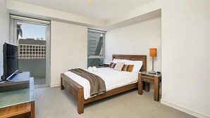 A hotel room with a bed, bedside table, lamp, and a desk with a chair. - North Sydney - BS901 Berry Street - Modern 1BR with Balcony in the Heart of North Sydney CBD (North Sydney)