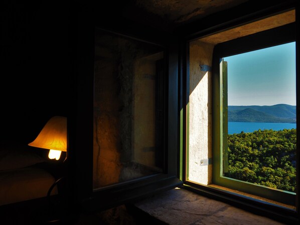 Una habitación con un amplio ventanal con vistas a un lago y colinas boscosas.