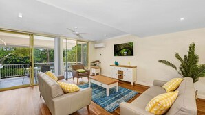Un salon spacieux avec un balcon, un ventilateur de plafond et un tableau représentant un pont.