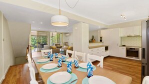 Une cuisine moderne avec des meubles blancs, un coin repas doté d’une table en bois pour quatre personnes et un balcon aménagé avec du mobilier d’extérieur.