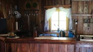 Une cuisine rustique avec des murs en bois, un plan de travail en bois et une fenêtre ornée de rideaux blancs.