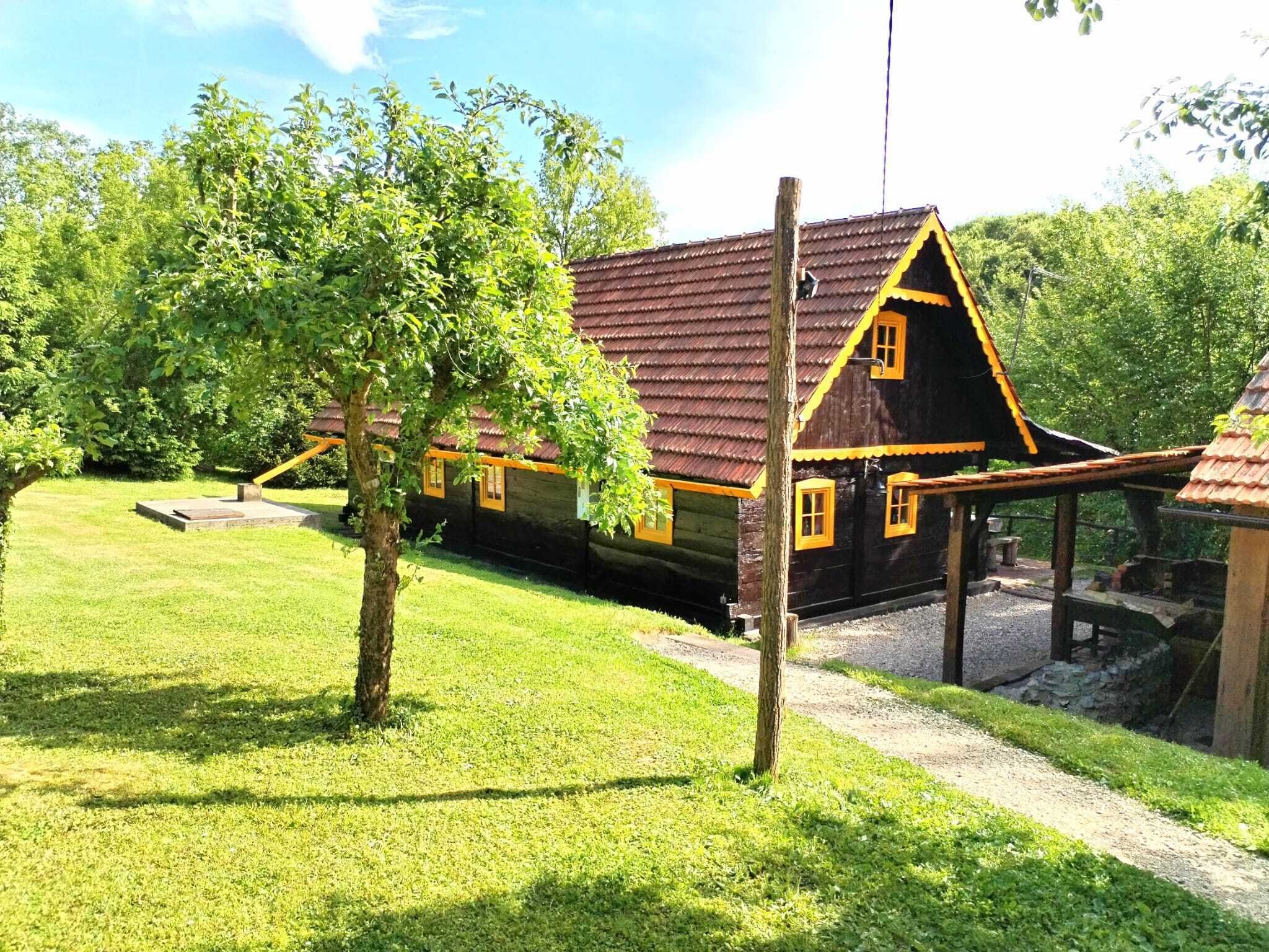 A traditional wooden house with a sloped roof, surrounded by a well-maintained lawn and trees.