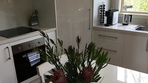 Eine moderne Küche mit weißen Schränken, einem Edelstahlbackofen, einer schwarzen Kochplatte und einem Fenster mit Blick auf Grünfläche.