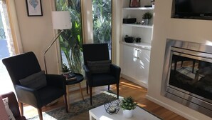 Ein Wohnzimmer mit zwei schwarzen Sesseln, einem weißen Couchtisch, einem Kamin und Blick auf Grünflächen.