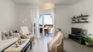 Una sala de estar moderna con sofá, sillón, puf, mesa de centro, televisor y estanterías con plantas.