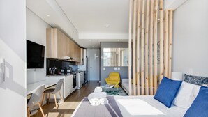 A modern hotel room with a bed, a desk, a chair, a sofa, and a kitchen area. - Backup-Powered City Apartment with Breathtaking Views on Popular Bree Street  (Cape Town)