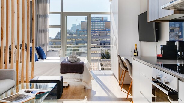A modern apartment with a balcony, a kitchen, and a living area with a sofa and a coffee table. - Backup-Powered City Apartment with Breathtaking Views on Popular Bree Street  (Cape Town)