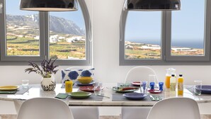 Una mesa de comedor con platos, vasos y un jarrón de flores, con vistas a un paisaje montañoso a través de ventanales arqueados.