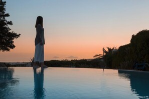 A person standing at the edge of a swimming pool during sunset.