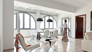Un amplio salón con una mesa de comedor, sillas blancas y un sofá.