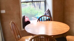 A dining area with a round wooden table and four chairs. A window with a view of trees is visible.
