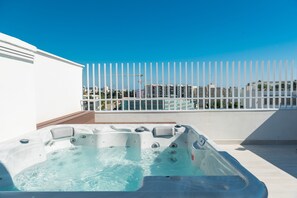 Un bain à remous sur une terrasse sur le toit, avec une clôture blanche et des bâtiments en arrière-plan.
