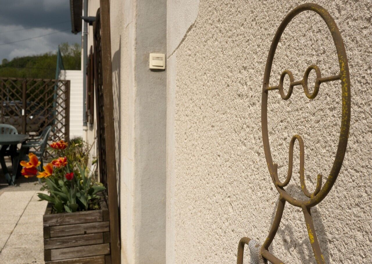 L’extérieur d’un bâtiment présente un mur en béton, un élément décoratif en métal et un jardinier en bois orné de fleurs.