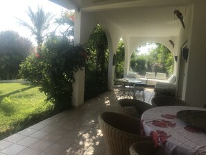 An outdoor patio area with a tiled floor, wicker furniture, and a view of a garden with trees and a lawn. - Superbe villa méditerranéenne spacieuse,lumineuse,calme, piscine, jacuzzi, parc, (Cabestany)