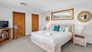 Un dormitorio con cama, mesitas de noche, una estantería, un ventilador y televisor.