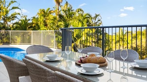 Un espacio exterior para comer con piscina, mobiliario de mimbre y vistas a palmeras.