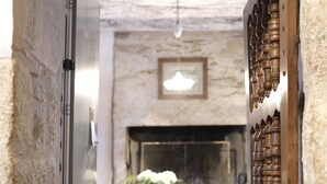 Un estrecho pasillo con una pared de piedra rústica, una puerta de madera con tallas intrincadas y un comedor al fondo con mantel y sillas rojas.