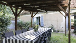 Un área de comedor al aire libre techada, con mantel a cuadros, sillas y luces colgantes.