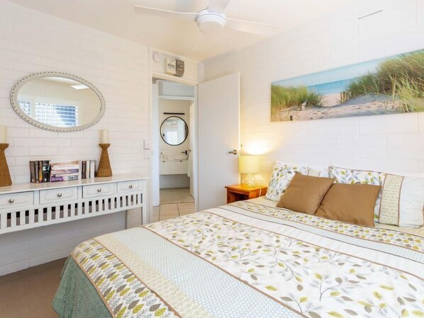A bedroom with a bed, a dresser, a mirror, and a painting on the wall. - Neat & Tidy unit, centrally located in the heart of Cotton Tree. (Sunshine Coast)