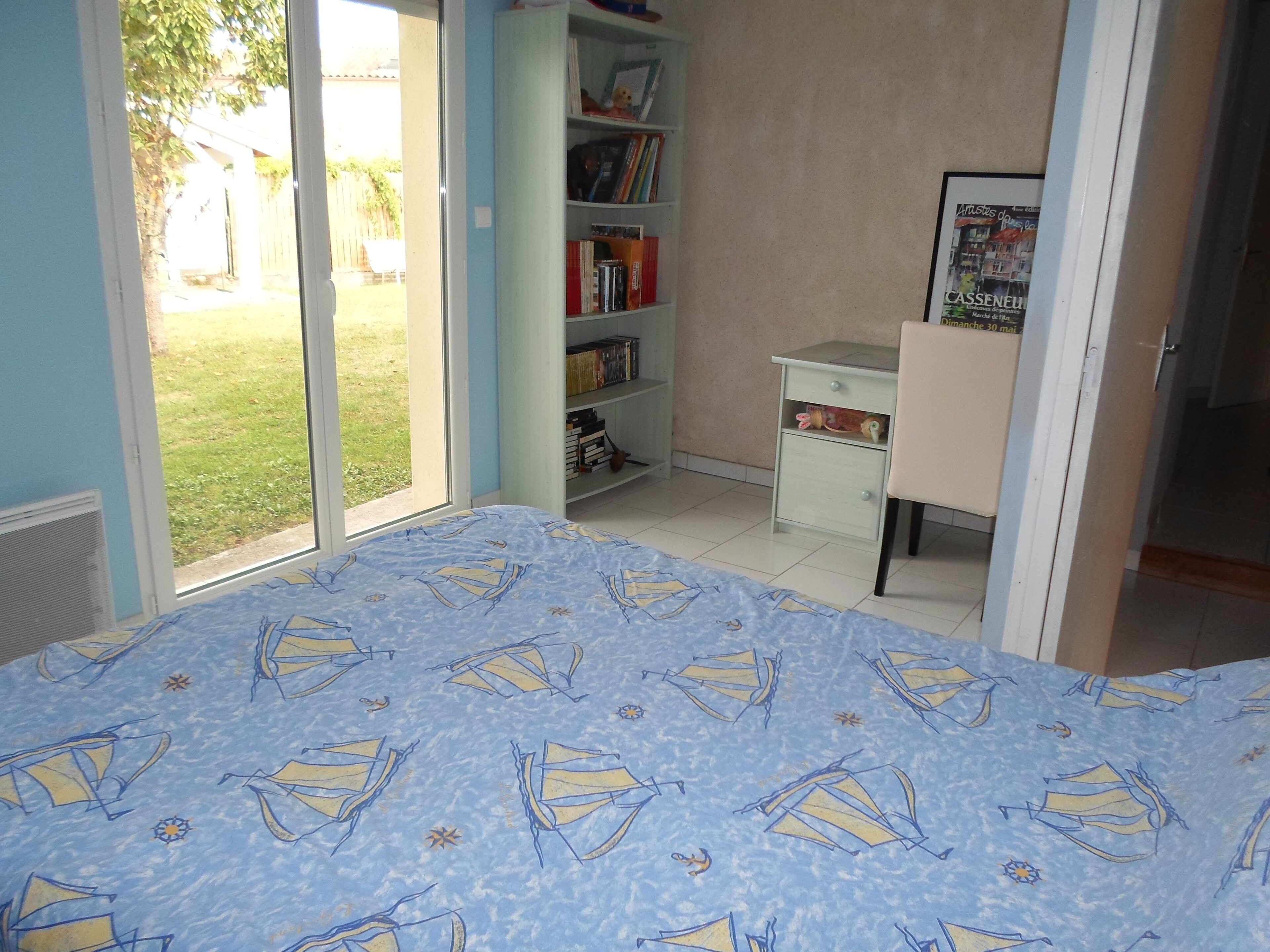 A bedroom with a bed, a desk, a bookshelf, and a door leading to a balcony.