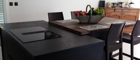 Une cuisine moderne dotée d’un grand îlot central, de meubles de rangement aux couleurs sombres et d’un luminaire suspendu.
