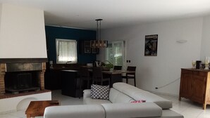 A modern living room with a grey sectional sofa, a fireplace, a dining area, and a kitchen in the background. - Furnished one-storey villa with 8 sleepings with a private pool (Bias)