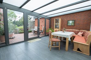 A conservatory with a glass door leading to a garden, a dining table with chairs, and a sofa. - Apartment Helene EG 35179 - Apartments Engelmann 35107 OG and Helene 35179 EC (Holtland)