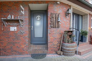 A brick building with a dark blue door, a small porch, and a wooden barrel planter. - Apartment Helene EG 35179 - Apartments Engelmann 35107 OG and Helene 35179 EC (Holtland)