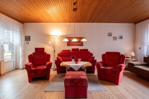 Ein Wohnzimmer mit Holzboden, rotem Mobiliar, einem Tisch mit einer Vase und Wandbildern.
