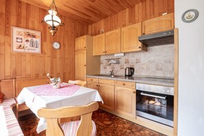A cozy wooden cabin with a dining area, wooden cabinets, a stove, and a clock on the wall. - Apartment Helene EG 35179 - Apartments Engelmann 35107 OG and Helene 35179 EC (Holtland)