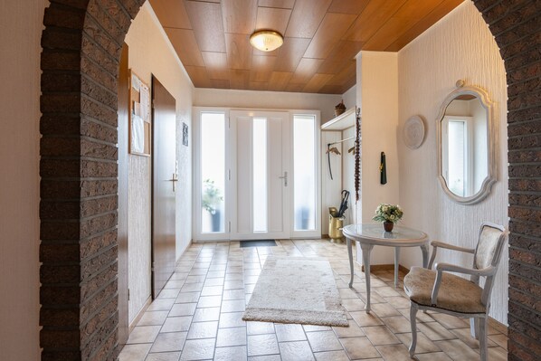 A hallway with a tiled floor, a rug, a chair, a table, and a mirror.