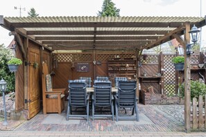 Eine Außenpatio mit einer Holz-Pergola, einem Tisch mit Stühlen und einem Backsteinweg.