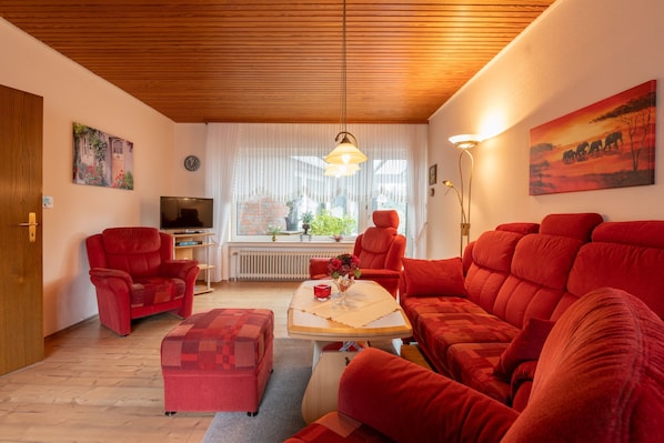 Sala de estar com móveis vermelhos, uma televisão e um quadro de elefantes.