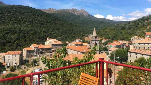 Un village aux bâtiments en pierre et à l’église, entouré de montagnes.