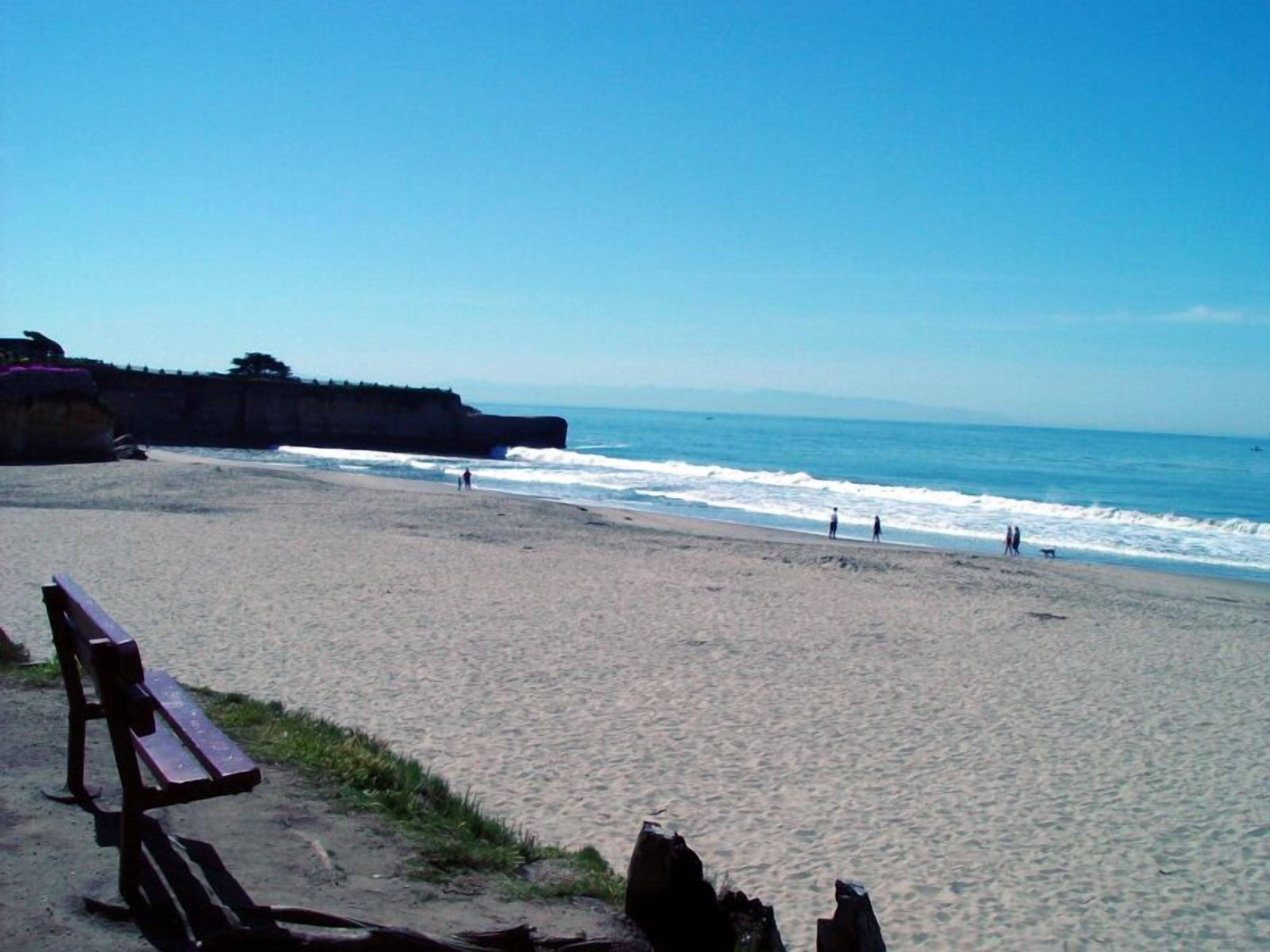 A beach with a wooden bench and a rocky cliff in the background.