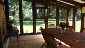 A wooden dining table with chairs, large windows, and a view of a green lawn. - Typical house from the Landes (Linxe)