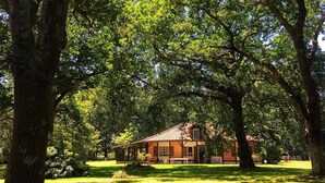 A rustic house with a brick exterior, surrounded by lush green trees and grass. - Typical house from the Landes (Linxe)