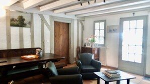 A room with a wooden bench, a black armchair, a small table, and a window with a view. - Typical house from the Landes (Linxe)