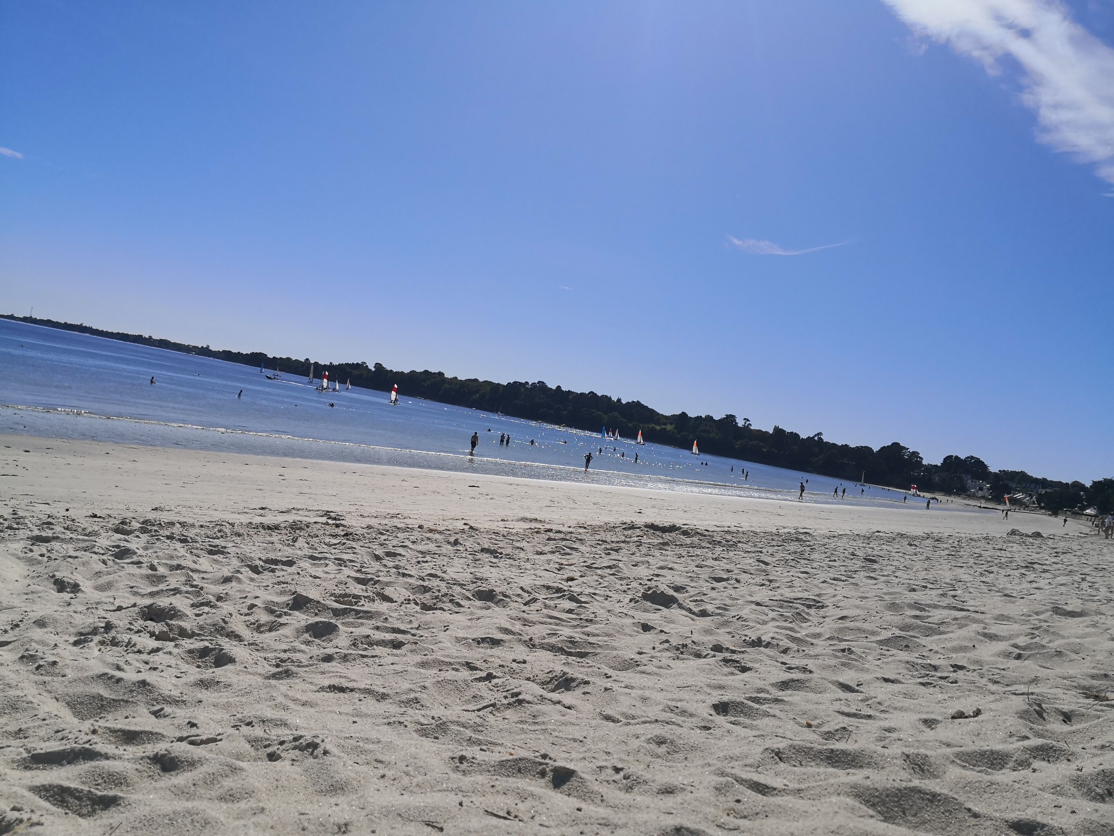 Una spiaggia sabbiosa con acqua cristallina, alcune persone e barche a vela.