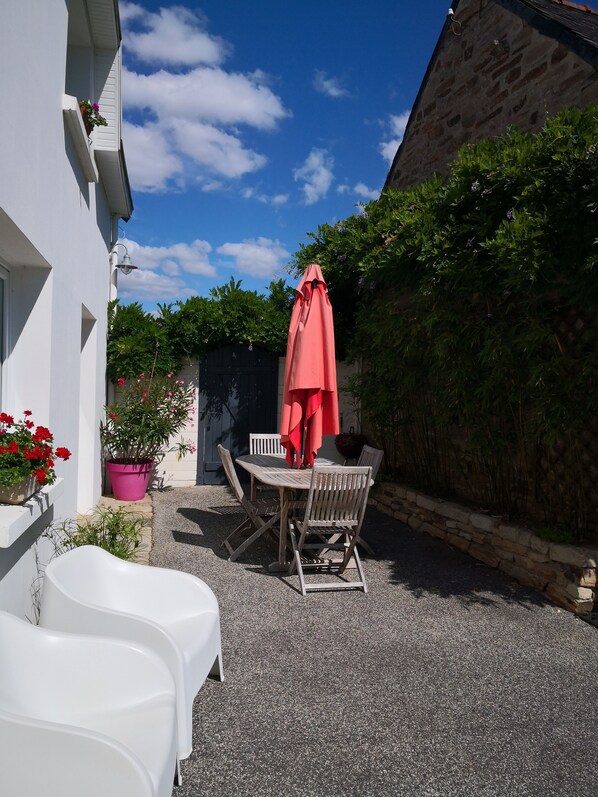 A patio with a table and chairs, a red umbrella, and potted plants.
