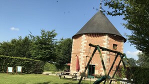 Une tour en briques surmontée d’un toit conique, entourée d’une pelouse où se trouvent une balançoire et des tables de pique-nique.