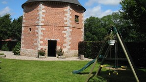 Une tour en briques surmontée d’un toit conique, une balançoire et une petite porte.