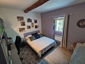 Ein Schlafzimmer mit Bett, Schreibtisch, Stuhl, Fenster mit Vorhängen und Wandbildern.